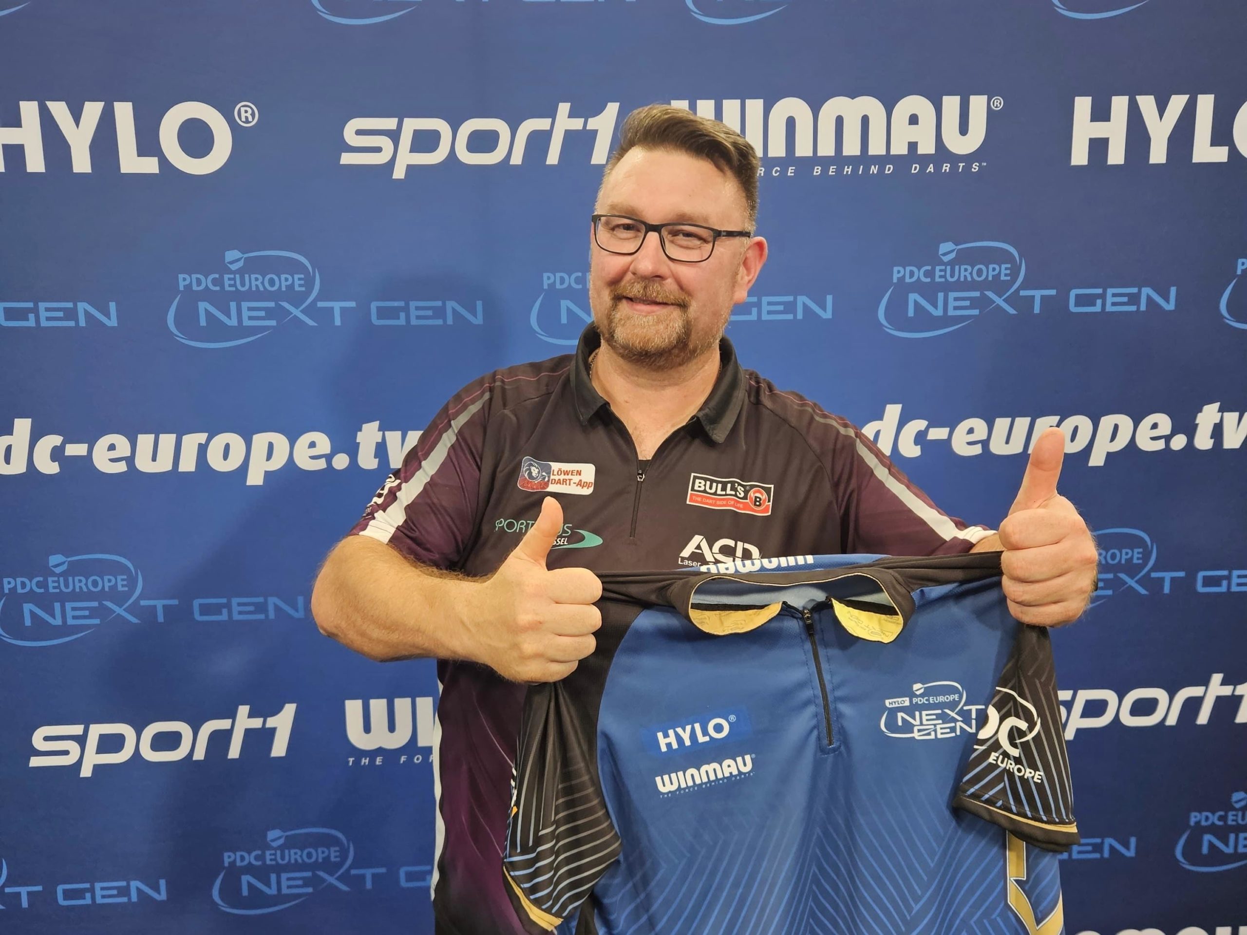 Dragutin Horvat hält als Sieger der PDC Europe Next Gen lächelnd das Gewinnertrikot mit Daumen nach oben